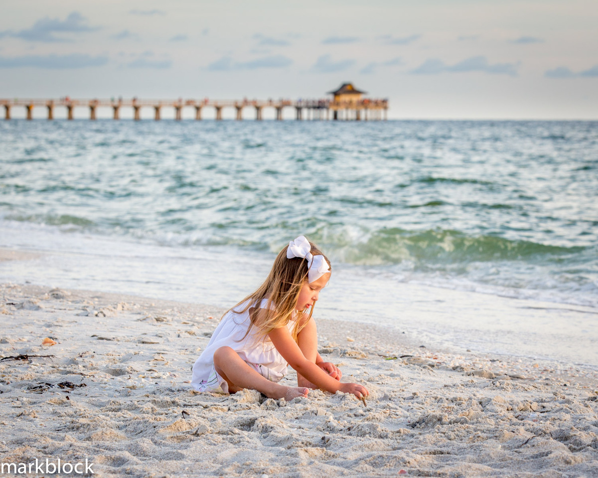 Photo of child sitting on beach with Naples Pier in background by Mark Block Photography